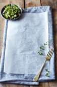 A grey tea towel and baking paper on a rustic wooden table