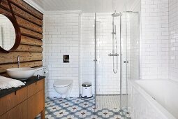 Badezimmer mit rustikaler Holzbohlenwand, Badewanne und verglastem Duschbereich