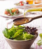 Öl auf Holzlöffel über gemischten Salat gießen