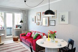 Wohnzimmer mit rundem weißem Esstisch vor rotem Polstersofa und Bildergalerie