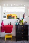 Red sink and black chest of drawers below mirror on wall