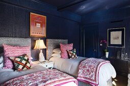 Twin beds with upholstered headboards and patterned scatter cushions in eclectic bedroom with dark blue walls