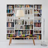 Weißes Bücherregal in Wandnische hinter Holzbank und Designer-Stehleuchte