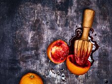 Juiced blood oranges with a wooden citrus juicer on a metal surface