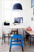 Dining and working area below window in period apartment; blue step-stool and table below black pendant lamp