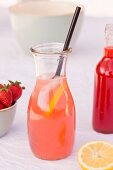 A carafe of homemade rhubarb and strawberry lemonade with lemons