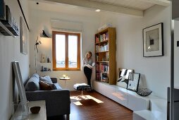 Woman reading between bookcase and windor in renovated living room