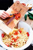 A woman adding tomatoes to a pasta salad