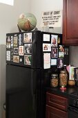 Globe and sign on top of black fridge decorated with photos in corner of kitchen