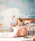 Young woman on double bed in front of studio wall with sky motif