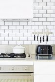 White tiled kitchen with stainless steel worktop, gas stove and black toaster under magnetic bar for knives