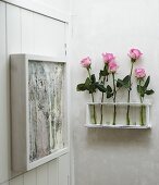 Roses in test tubes in wall bracket next to artwork