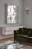 Glass coffee table, velvet sofa, white floating sideboard and mirrored wall-mounted cabinet in corner of living room