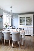 Pale grey upholstered chairs around wooden table below chandelier in traditional, Scandinavian-style dining room