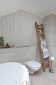 Pale grey tiles on floor and false wall in bathroom with towels on ladder next to toilet