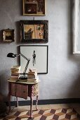 Antique, fabric-covered bedside table below pictures on wall