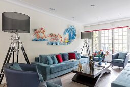 Two standard lamps with transparent lampshades flanking blue sofa and artwork on wall of elegant lounge