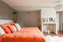 Doppelbett mit orangefarbener Bettwäsche in traditionellem Schlafzimmer mit gemauertem, stillgelegtem Kamin