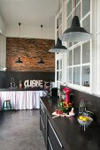 Black kitchen counters, brick wall, pendant lamps and charcoal concrete floor in loft apartment