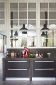 Black, concrete kitchen counter with drawers and kitchen utensils below interior windows in loft-style apartment