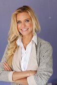 A young blonde woman wearing a white blouse and a grey shirt jacket