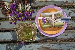Gedeck mit Stoffserviette, Besteck und lila Krokussen auf Holzuntergrund