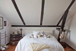 Doppelbett mit Teddybären und Dekokissen unter Dachschräge neben nostalgischem Kofferstapel in renoviertem Bauernhaus