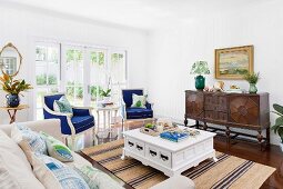 Elegantes Wohnzimmer mit blau gepolsterten Armlehnstühlen, Antikmöbeln und Landhausflair