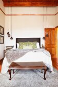 Double bed and bedroom bench made from exotic wood in high-ceilinged bedroom with pendant lamps