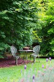 Romantischer Gartenplatz mit Tisch und zwei verzierten Eisen-Gartenstühlen im Antikstil