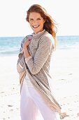 Junge brünette Frau in langer Shirtjacke und dünner Hose am Strand