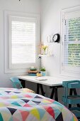 Desk with white desk top and black wooden trestles next to the bed