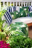 Sunny terrace with green plants, pouf and cozy upholstered sofa with various pillows