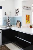 Black fitted kitchen units with white worksurface and splashback of pale blue wall tiles