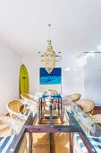 Rattan armchairs around long dining table with glass top, surfboard and picture with sea motif in background