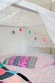 Romantisches Bett in Mädchenzimmer mit weißem Baldachin, bunter Häkelgirlande und pastellfarbener Bettwäsche