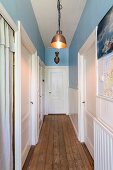 Narrow hallway with rustic wooden floor, white interior doors and blue-painted walls