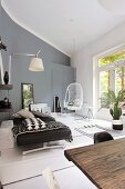Modernes Wohnzimmer in Grautönen, mit Tagesbett, Hängestuhl, Wandleuchte und Pflanzen, im Vodergrund rustikaler Holztisch