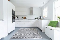 Storage bench below window and rug with graphical pattern in elegant white fitted kitchen