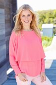 A young blonde woman wearing a long-sleeved, layer-look top and pink trousers