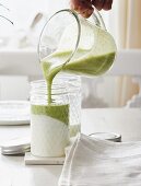 A green smoothie with avocado and matcha being poured over yoghurt in a glass