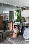 Hand-shaped designer chair at round table in front of mirrored cupboards