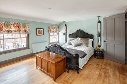 Vintage bed with wickerwork frame and wooden trunk in renovated bedroom with oak floor