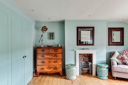 Antique chest of drawers next to traditional fireplace and armchair in bedroom