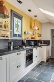 White kitchen counter with granite worksurface below shelves mounted on yellow wall