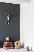 Various hunting trophies on black wall above stack of retro suitcases and wooden sculpture