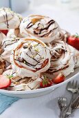 Various meringues with chocolate sauce, strawberries and pistachio nuts on a plate