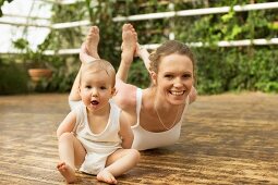 A woman practising yoga with her baby sitting beside her