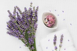 A bouquet of lavender, lavender and rose petal soap in a bowl with lavender flowers on a white towel