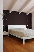 Weißes Bett vor schwarzer Wand im Dachzimmer